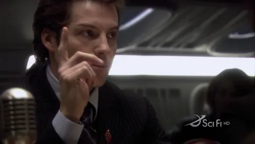 Un hombre trajeado frente a un micrófono en Battlestar Galactica
