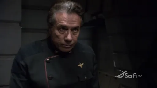 Adama con expresión seria en un pasillo oscuro en Battlestar Galactica