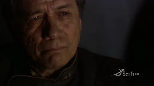 Primer plano del almirante Adama emocionado en la penumbra en Battlestar Galactica