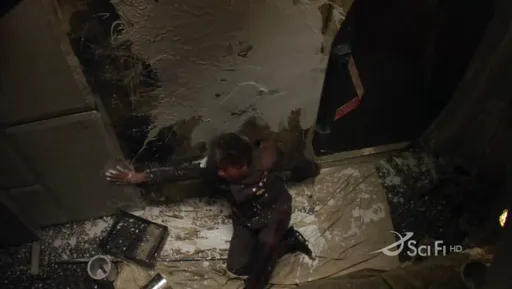 Un hombre tirado entre escombros en un pasillo destrozado del Galactica