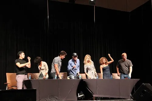 Los actores del panel de Battlestar Galactica de pie tras la mesa en el escenario de la Dragon Con