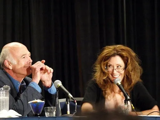 Michael Hogan y Mary McDonnell sentados juntos en la mesa del panel, ella sonriendo