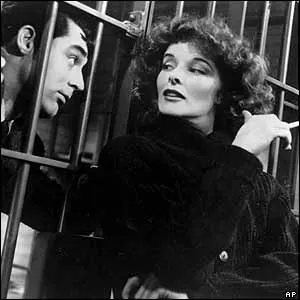 Katharine Hepburn con un cigarro junto a un hombre tras unas rejas en La fiera de mi niña