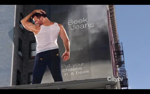 Un hombre en camiseta posando en una valla publicitaria de vaqueros Beek